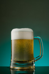 Glass of beer with foam on blue background