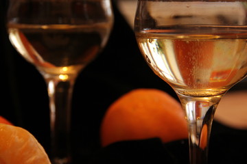 two glasses of champagne stand on a black background with tangerines. Bubbles of sparkling wine in a glass.