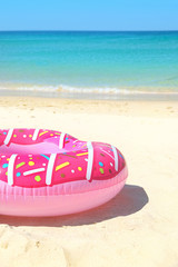 Hipster Pink inflatable donut swimming ring on sand at sea coast, sunny day. happy childhood, Summer travel, vacation time concept.