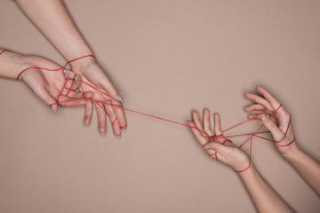 Top view of hands of women wrapped in red thread on beige background