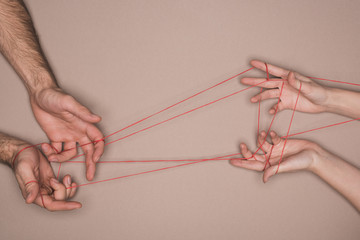 Top view of man and woman holding red string on beige background