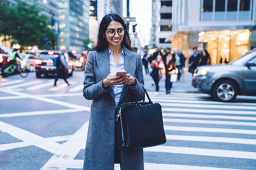 Happy female standing on crosswalk with smartphone
