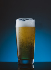 Glass of beer with foam on blue background