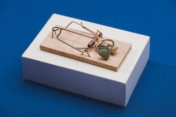 Jewellery ring with precious stone in mouse trap on white block on blue background