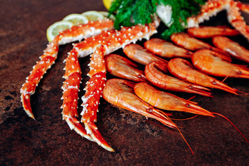On the table are shrimp, crab, lemon and herbs. Table of reddish color.