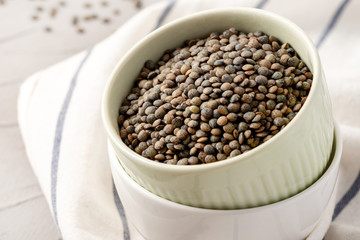 French green lentils in a bowl on the table, closeup. Dry unprepared green lentils.