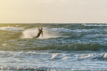Wave kitesurfer riding a turn in the waves of the baltic sea in beautiful yellow sunset conditions