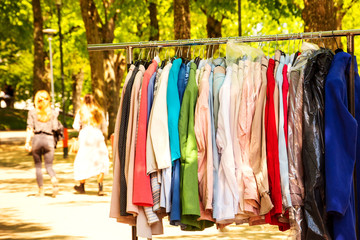 Elegant vintage colorful clothes for sale at street market in France in sunny spring day. Silhouettes of two blurry young woman walking at background - casual and retro style looks.