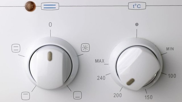 Hand turning on two round temperature oven switches of white electric stove in home kitchen