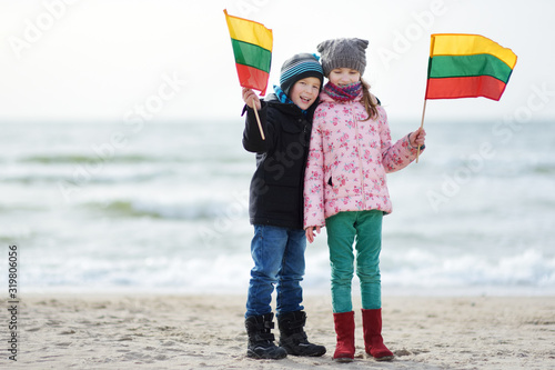 Adorable little brother and sister celebrating Lithuanian Independence Day holding tricolor Lithuanian flags