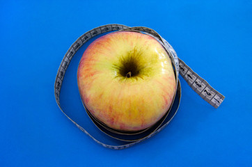 measuring tape wrapping an apple on a blue background. The concept of weight loss, diet.