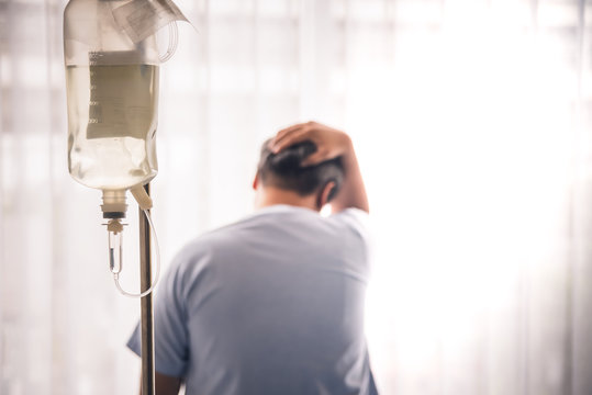 Blurred soft images of the male patient, Being stressed from the sickness and This image focuses on a saline bag hanging on the pole, to health insurance concept.