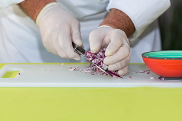 Chef picks up red onion dice with a knife