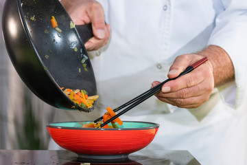 Chef uses chopsticks to move fried vegetables into a bowl