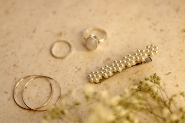 Fashionable accessories on pale pink background. Beret with pearls, silver gemstone ring and hoop earrings, with gypsophila flowers. Selective focus.