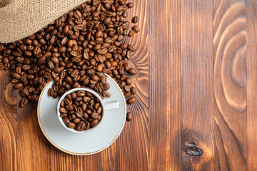 Roasted coffee beans in a white cup and knitted bag on a burnt wooden background. Copy space.