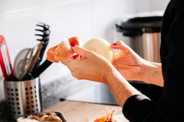 Obraz na płótnie Canvas A woman's hands peeling an onion in a kitchen.