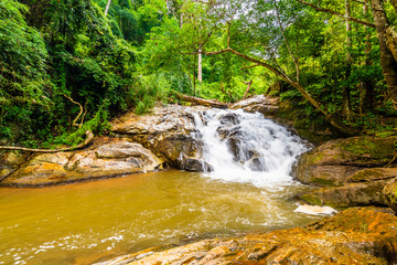 Beautiful waterfall Mae Sa, Thailand. Fresh and pure water stream is flowing on the rock stone ground in tropical rainforest. Fresh plants and trees above river. Vibrant colors in pure nature