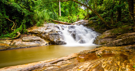 Obraz premium Beautiful waterfall Mae Sa, Thailand. Fresh and pure water stream is flowing on the rock stone ground in tropical rainforest. Fresh plants and trees above river. Vibrant colors in pure nature