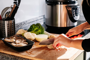 A woman's hands cutting mushrooms and vegetable onion cabbage and leeks in a kitchen
