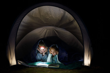 Girls reading a book with torch at night during summer holidays