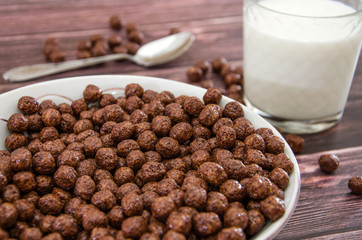 chocolate balls in a plate and a glass of milk. dry breakfast on a wooden background. .