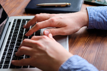 A man in a shirt works behind a laptop typing text.