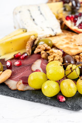 Food Platter With Truffle Cheese, Duck Breast, Brie Cheese, Pecan Nuts, Pomegranate Seeds, Grapes, Almonds, Honey, Olives and Crackers on White Marble Background