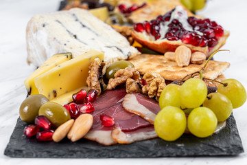 Food Platter With Truffle Cheese, Duck Breast, Brie Cheese, Pecan Nuts, Pomegranate Seeds, Grapes, Almonds, Honey, Olives and Crackers on White Marble Background