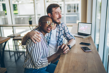 Happy diverse couple enjoying city view from large cafe window