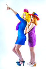 Holiday sale. Shocked girls in carnival clothes pointing index fingers at something. Girls in wigs...