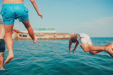 Group of happy crazy people having fun jumping in the sea water from boat. Friends jump in mid air...