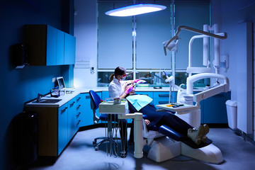 Female Dentist very carefully check up and repair tooth of his young female patient. Happy young woman sitting in dental chair at dentist office