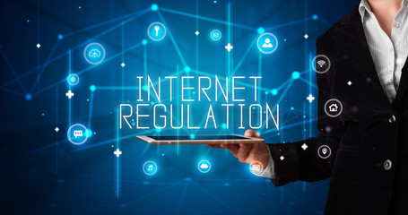 Young business person working on tablet and shows the digital sign: INTERNET REGULATION