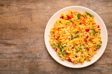 Tasty rice pilaf with vegetables on wooden table, top view. Space for text
