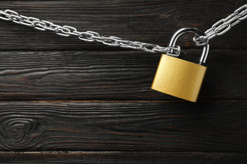 Steel padlock, chain and space for text on black wooden background, top view. Safety concept