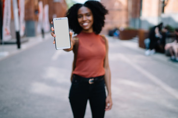 Bright African American woman showing phone walking in street