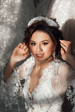 Beautiful bride on her wedding day. Wedding robe on bride. Smile and relax, young and beautiful. The bride straightens the crown. Bride with wedding makeup and hairstyle with crown