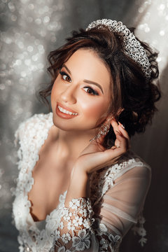 Beautiful Bride Portrait wedding makeup and hairstyle, girl in diamonds tiara, fashion bride gorgeous beauty, smiling happy bride portrait. Bride in white silk robe in her bedroom