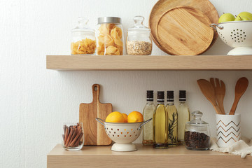 Wooden shelves with dishware and products on white wall. Kitchen interior idea