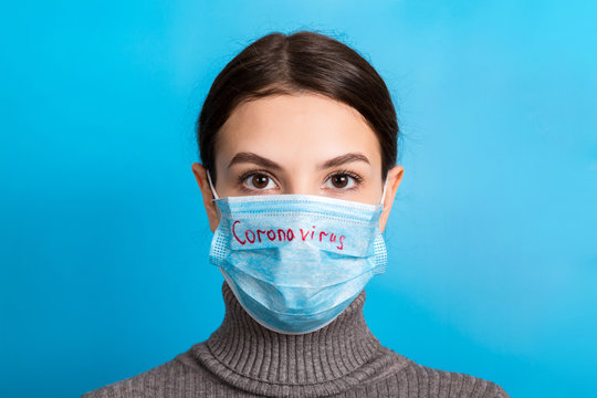 Portrait of pretty woman wearing medical mask with coronavirus text at blue background. Coronavirus concept. Respiratory protection