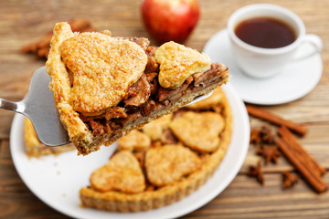 Closeup piece of homemade apple pie with cinnamon and cup of tea on wooden table. Shallow focus.