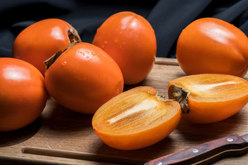 Fresh ripe persimmon fruit, winter fruit, cut on board and black background