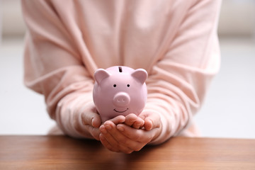 Woman with piggy bank at wooden table, closeup