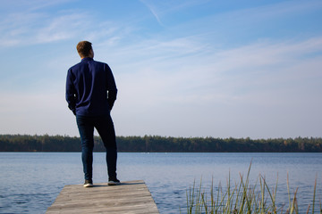  A man stands on a wooden bridge on a lake on a clear day. Blue sky and lake. Scenery