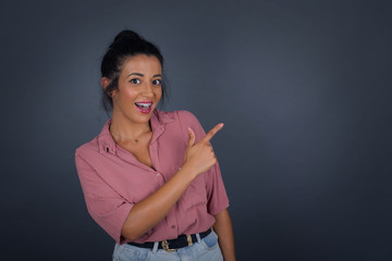 Fototapeta premium Look over there! Beautiful blonde caucasian woman pointing away and smiling to you while standing against grey background.