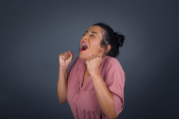 Beautiful young woman happy and excited expressing winning gesture. Successful and celebrating victory, triumphant, gray background.