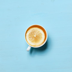 A cup of black tea with slice of lemon on pale blue background.