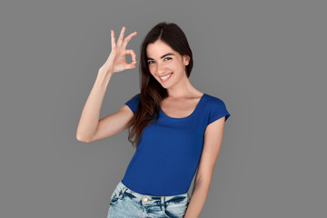 Young girl studio standing isolated on grey showing ok sign cheerful