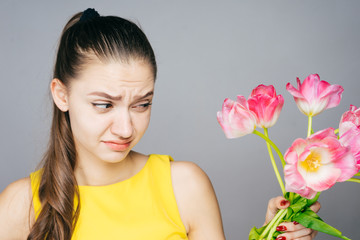 girl with resentment and light squeamishness looks at a bouquet of tulips in her hand